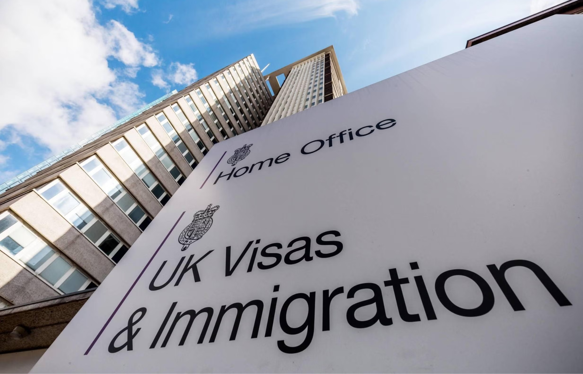 A Home Office "UK Visas & Immigration" sign against a building and blue sky.