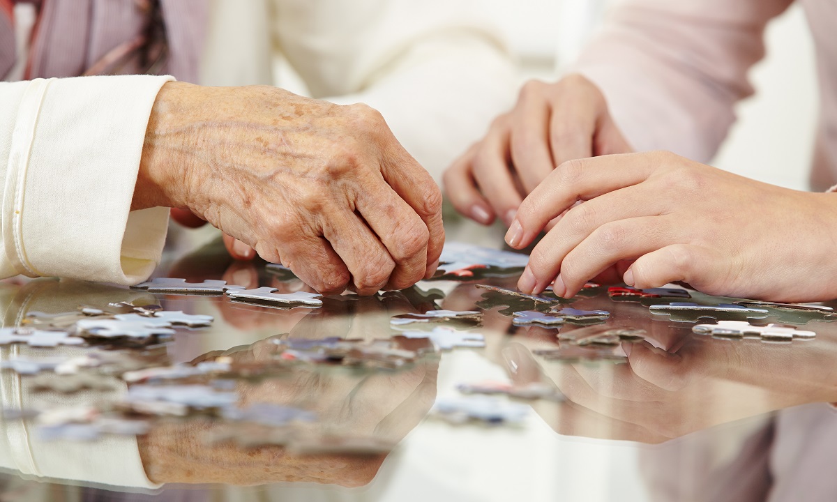 Close-up of an older person's hand and a younger person's hands working on a jigsaw puzzle together.