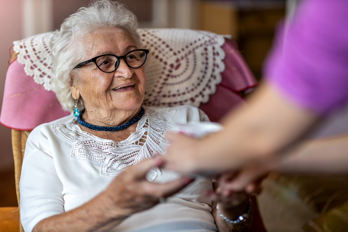 An older woman smiles while a care worker holds her hand.